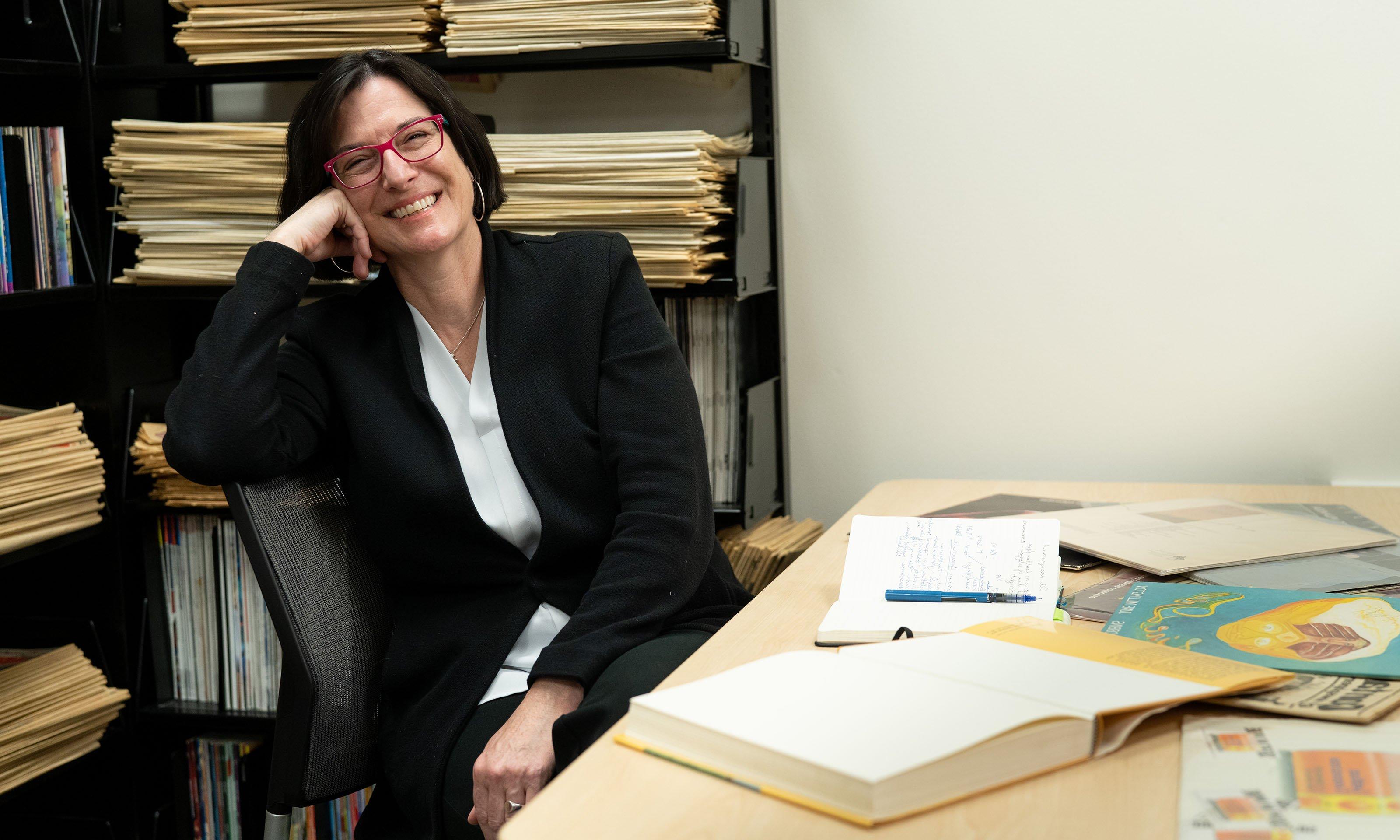 Woman sitting and smiling with record albums and books open on table