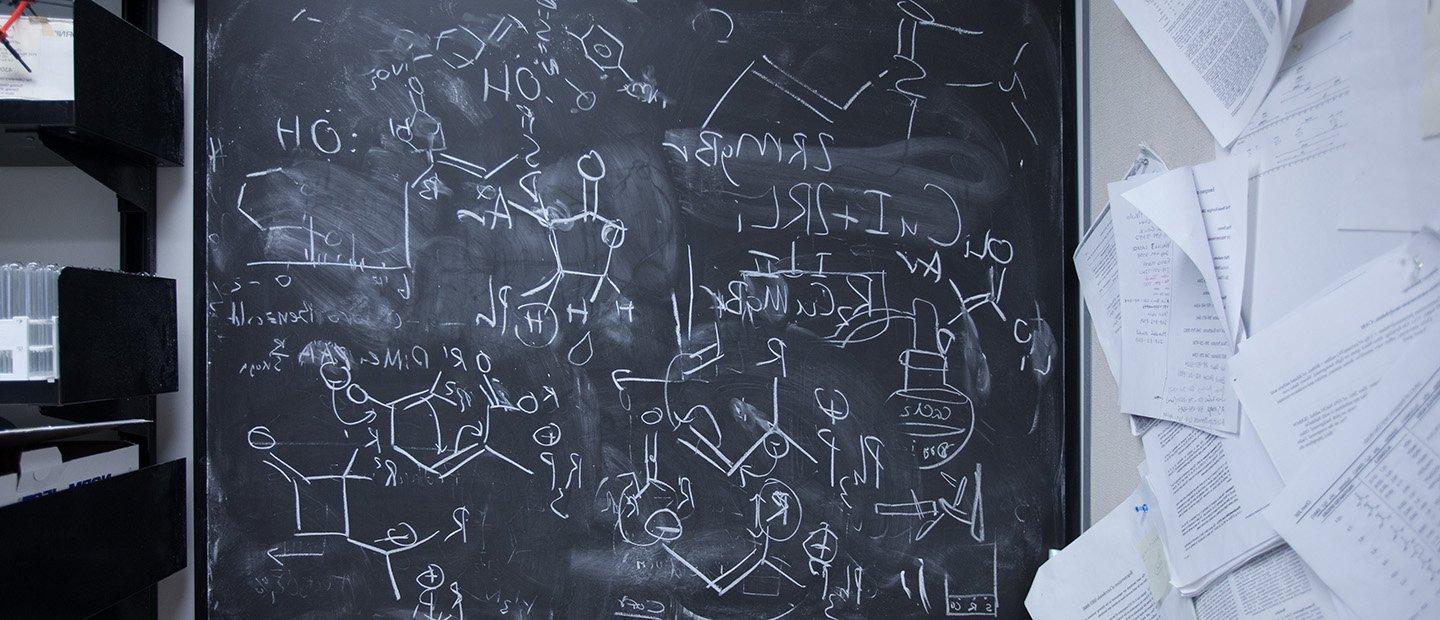 A chalkboard with chemical equations and diagrams written on it.